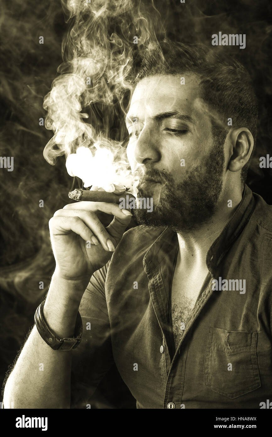 gangster smoking cigarette Man Smoking Cigar surrounded by Smoke / short bearded man with a gangster  look smoking cigar surrounded by smoke over dark background Stock Photo