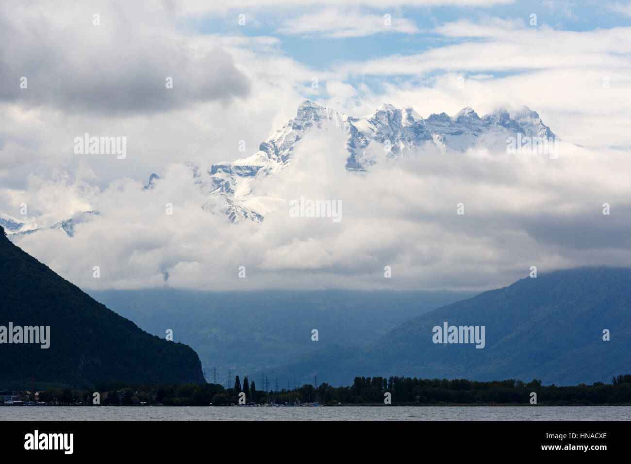 Snowy peaks of rocky mountains appeared from the clouds. Viewed from the town of Montreux closer located hills and Lake Geneva can be seen in the shad Stock Photo