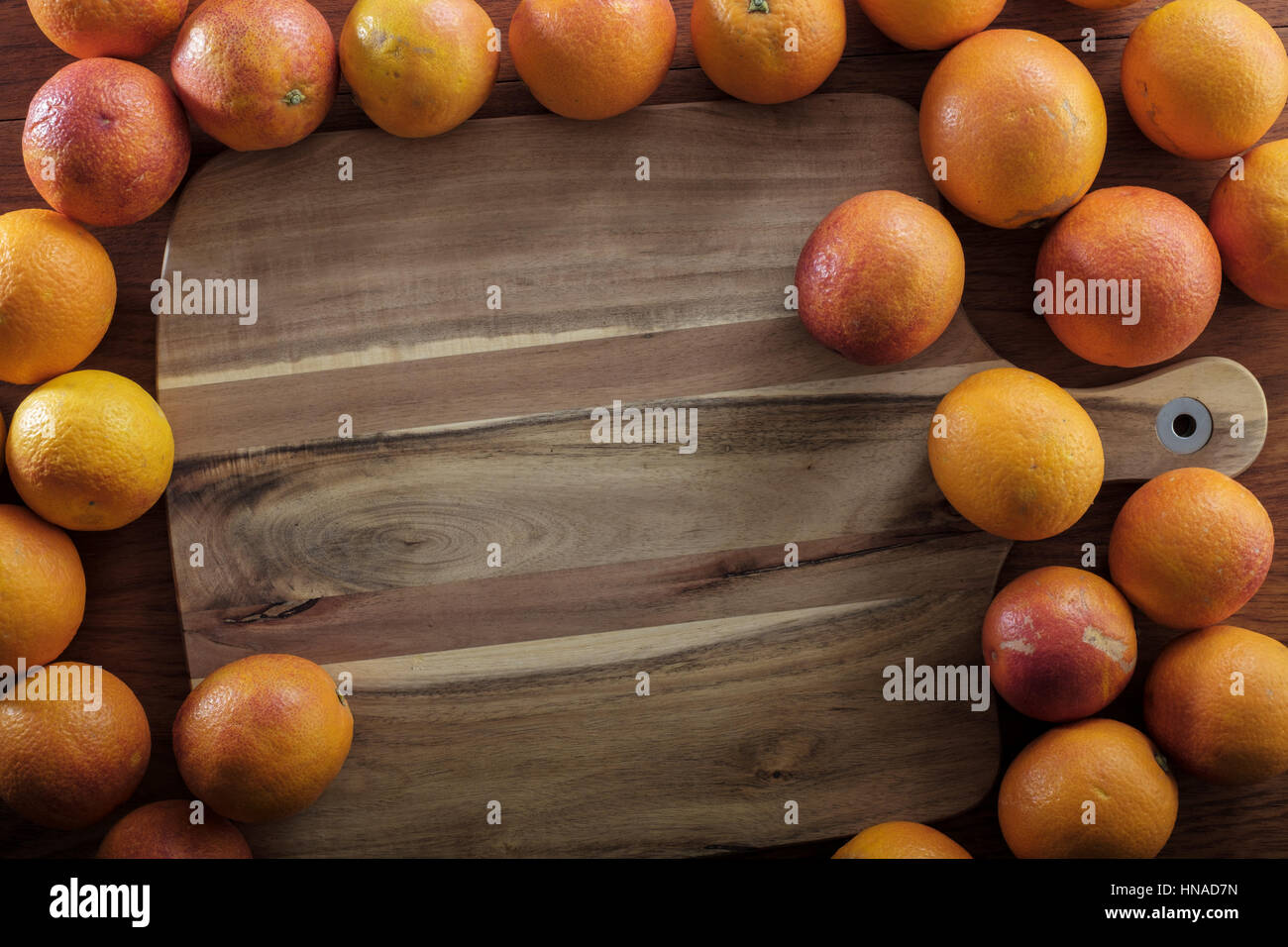 Oranges on wooden table around cutting board Stock Photo