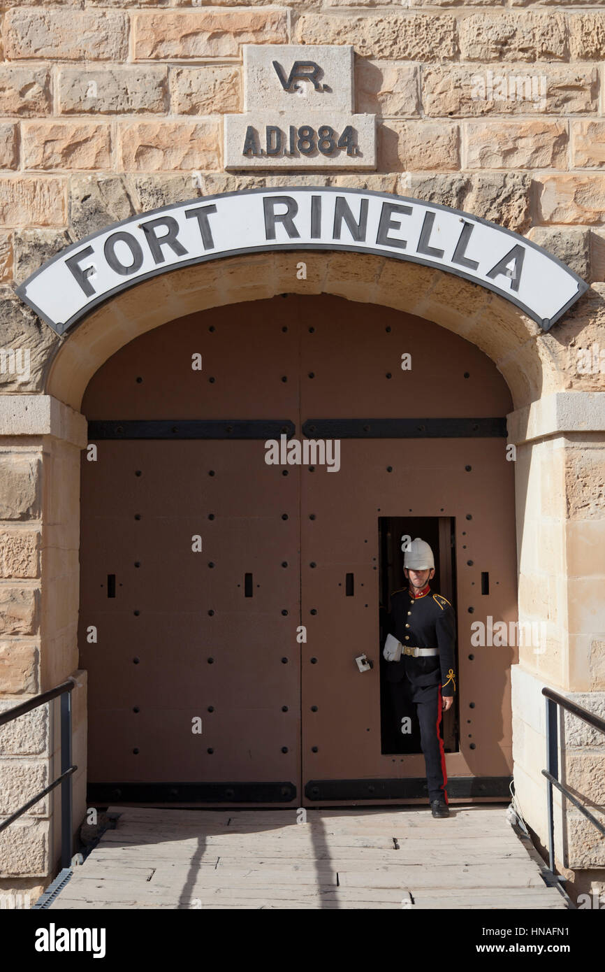 A site guide in period British military uniform stepping out of the main door of Fort Rinella in Malta. Stock Photo