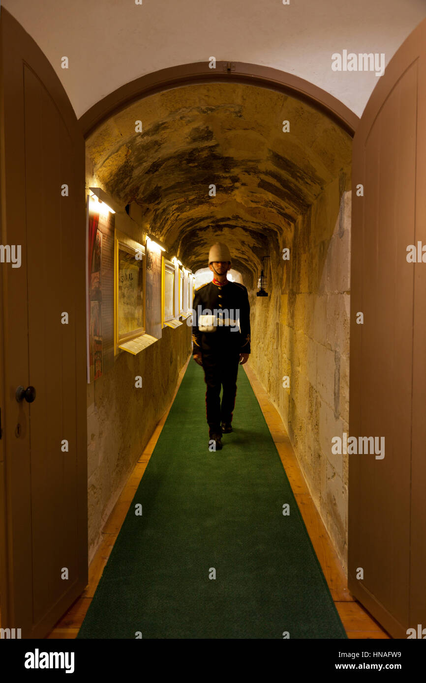 A site guide in historical British military uniform walks down a corridor tunneled through the thick walls of the nineteenth century Fort Rinella in M Stock Photo