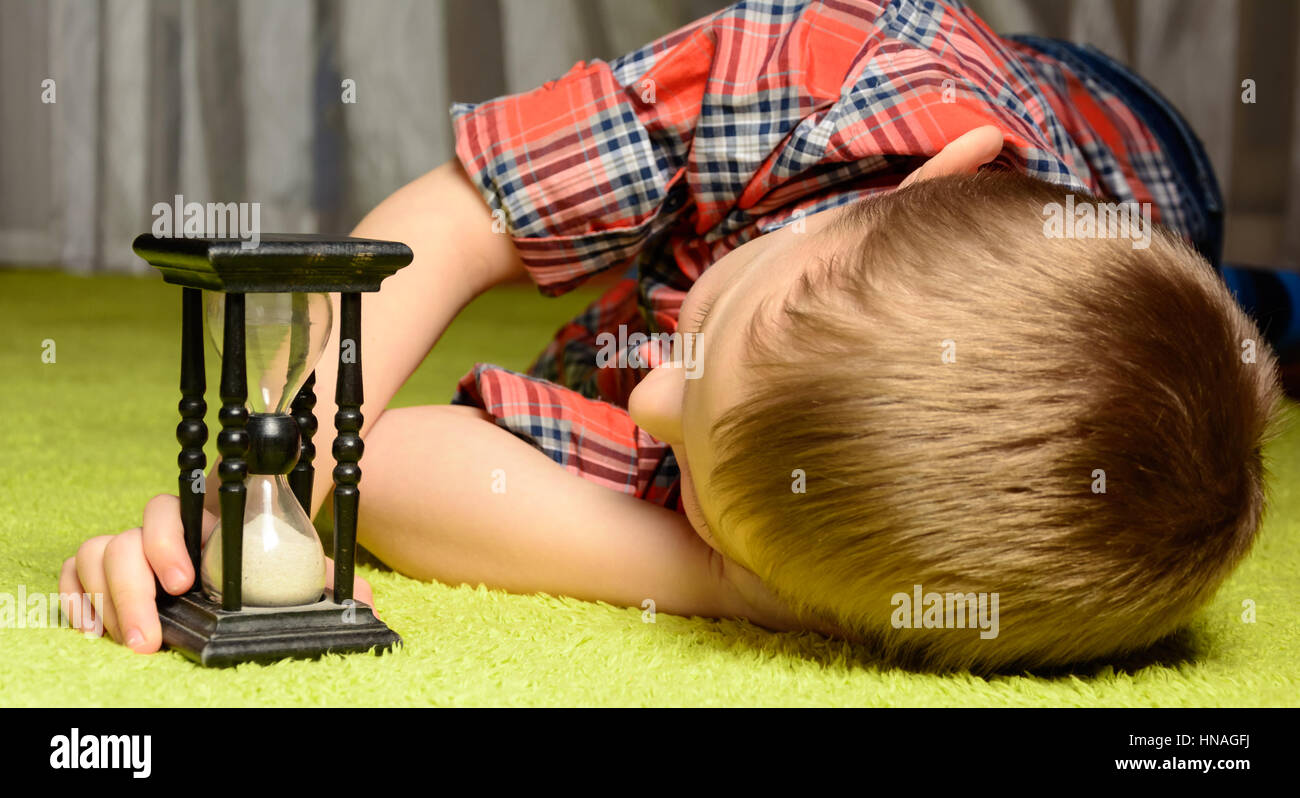 little boy lying on the floor and looking at hourglass Stock Photo