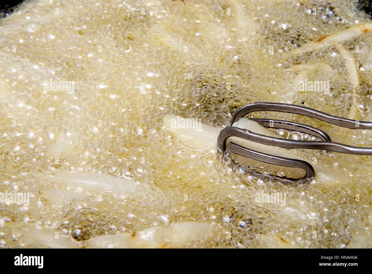 french fries frying in hot bubbling oil, tongs turning stirring during