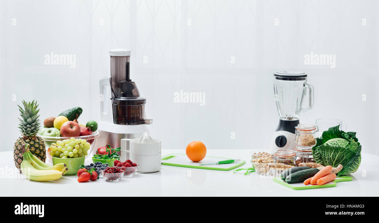 Kitchen table with fresh vegetables, fruit, seeds, blender and juicers; healthy diet and food preparation concept Stock Photo