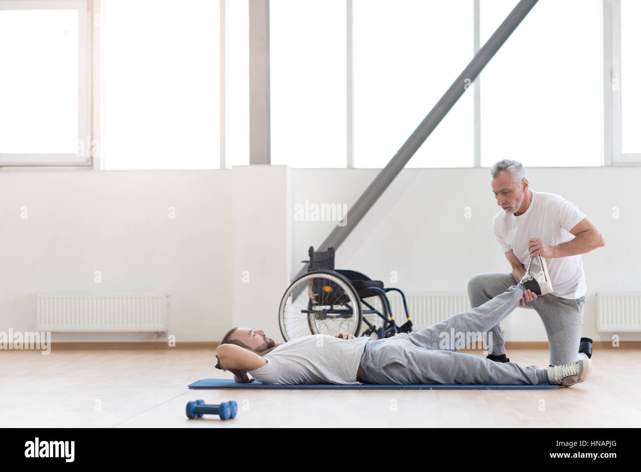 Skilled orthopedist working out with disabled patient in the gym Stock Photo