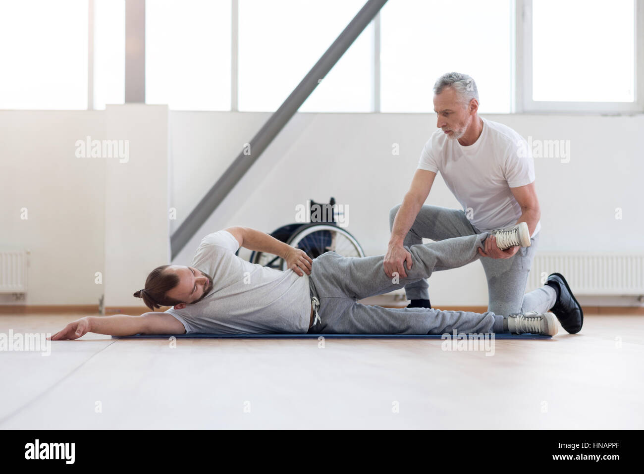 Concentrated physical therapist stretching the handicapped in the gym Stock Photo