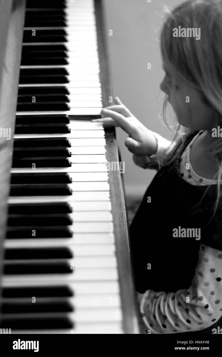 Side profile five year old child kid girl long hair sitting piano playing piano lesson music lessons learning music instrument education concept Stock Photo