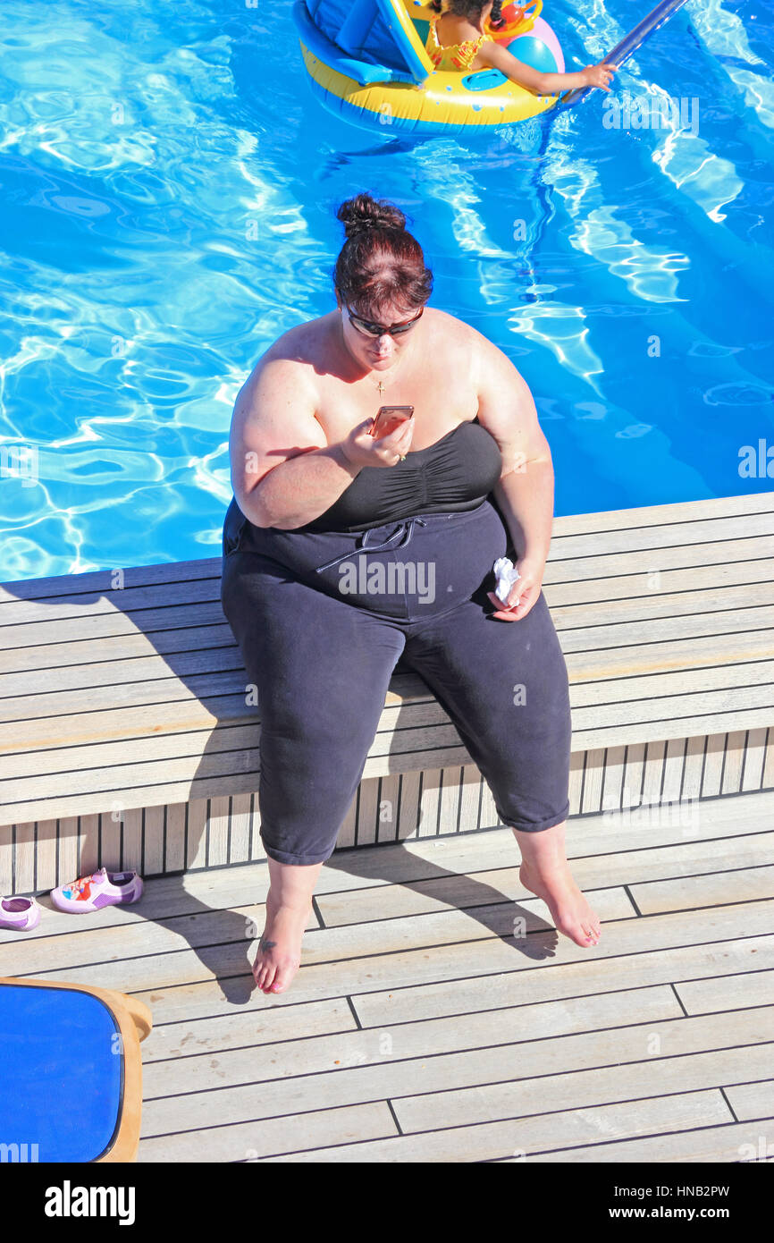Obese lady sat on edge of swimming pool Stock Photo