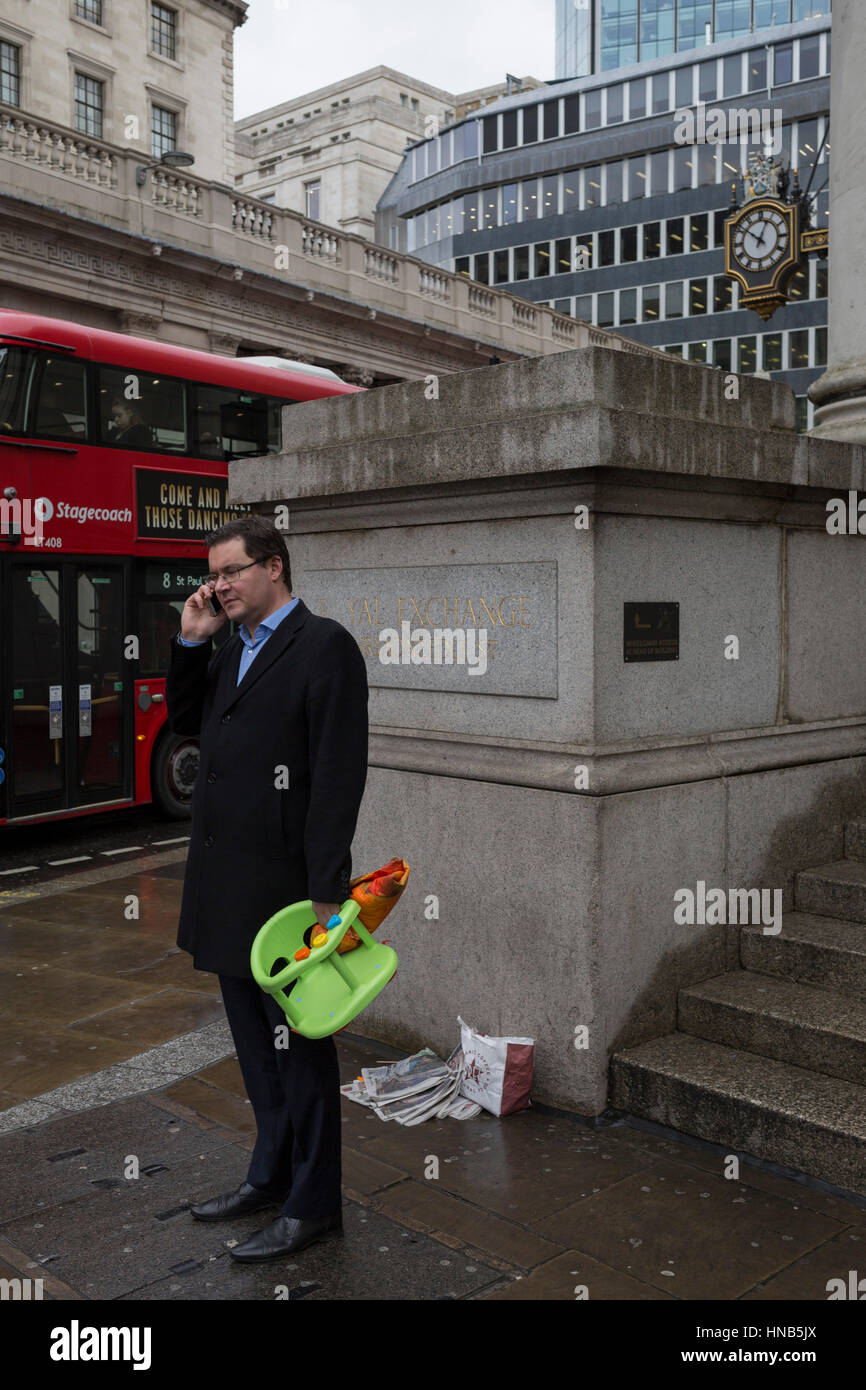 A businessman and father holds a bright green child's seat, on 2nd February 2017, in the City of London, England. Stock Photo