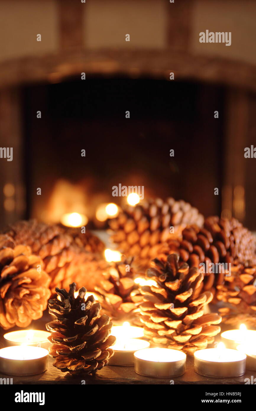Pine cones and candle light festive slate table top display in a cosy fireside setting of an English home at winter Stock Photo