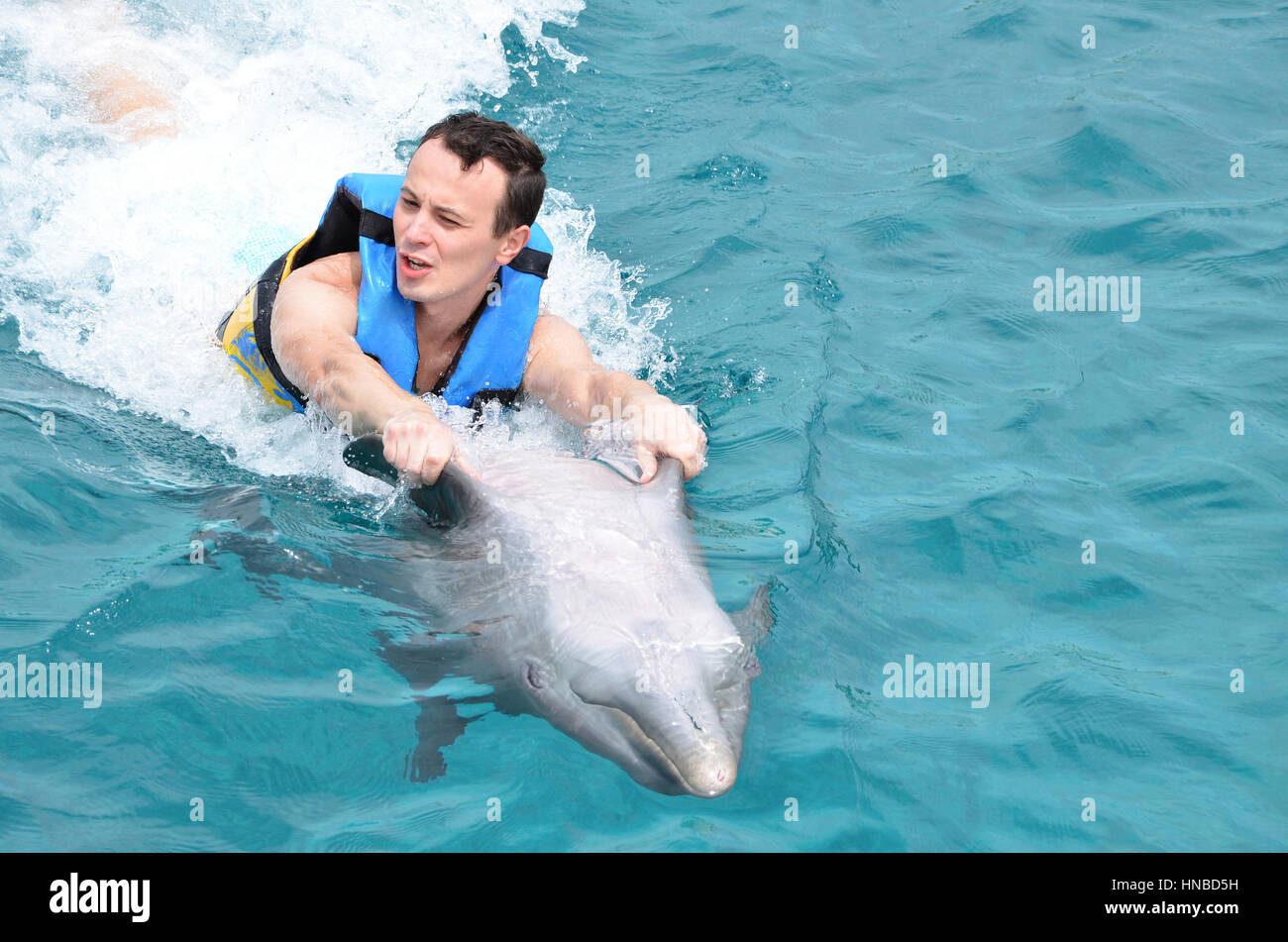 young man holding dolphin fin and ride on blue water ocean Stock Photo