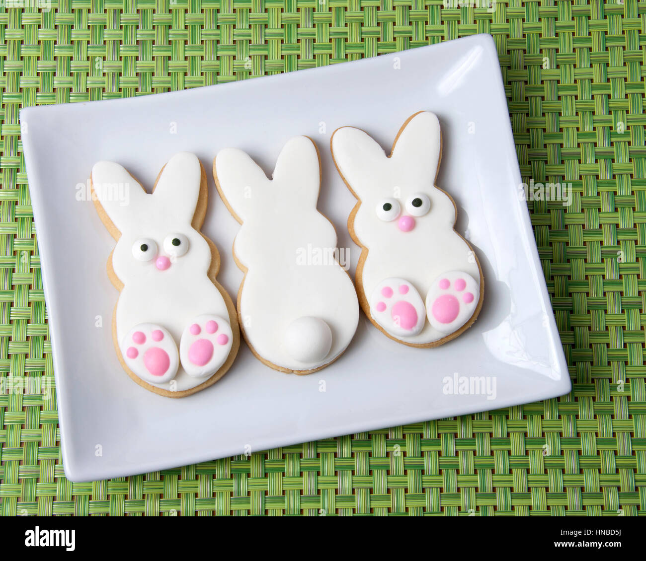 Easter Bunny Sugar Cookies on a plate with green place mat background. Marshmallow fondant covered cookie with candy feet, eyes and nose and tail. Stock Photo
