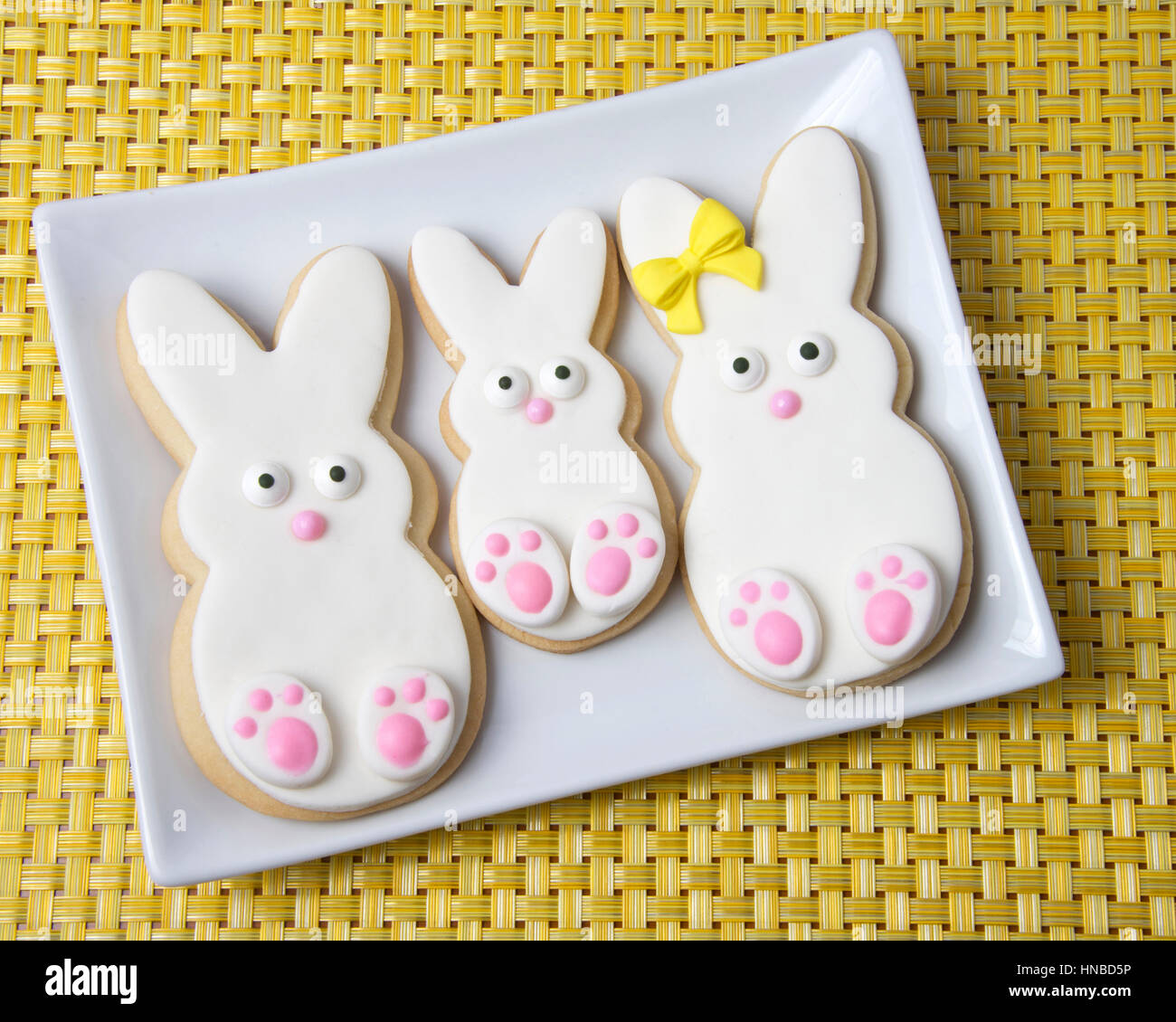 Easter Bunny Sugar Cookies on a plate with yellow place mat background. Marshmallow fondant covered cookie with candy feet, eyes and nose and tail. Stock Photo