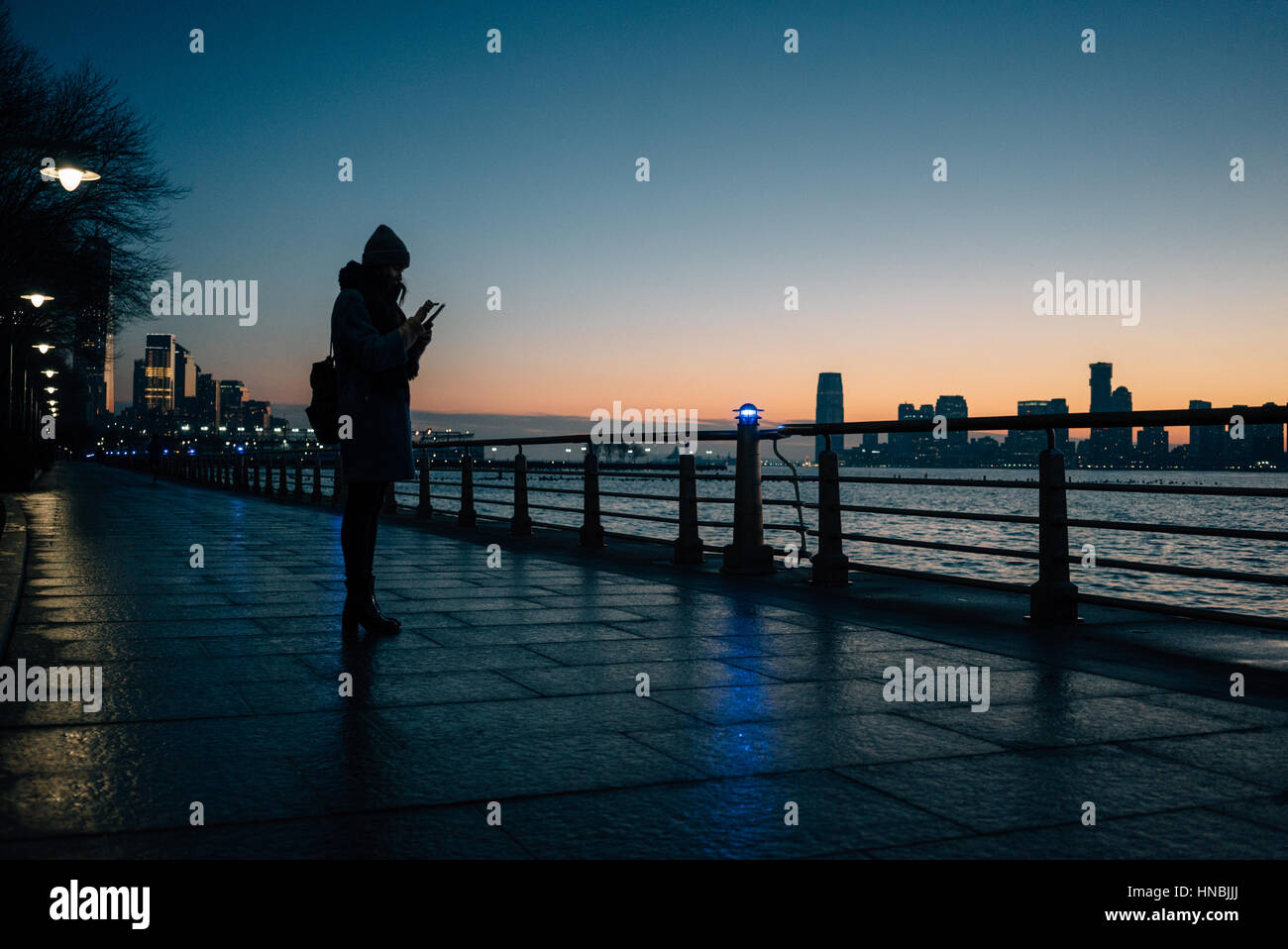 Side view silhouette of a woman standing on river pier and texting message during sunset Stock Photo