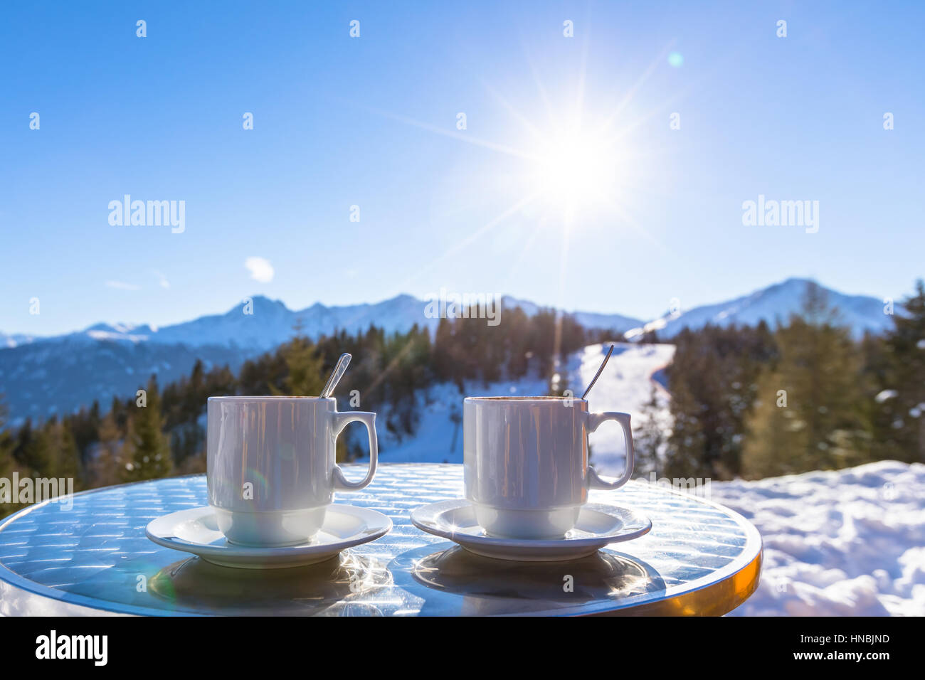 Two hot chocolate mugs on the terrace of an altitude restaurant in the mountain ski resort with beautiful sunny white winter background Stock Photo