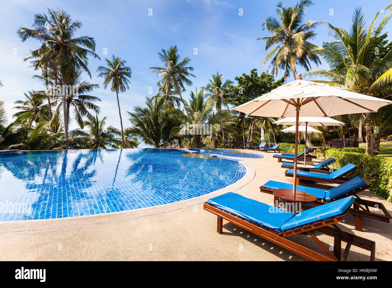 Beautiful tropical beach front hotel resort with swimming pool, sun-loungers and palm trees during a warm sunny day, paradise destination for vacation Stock Photo