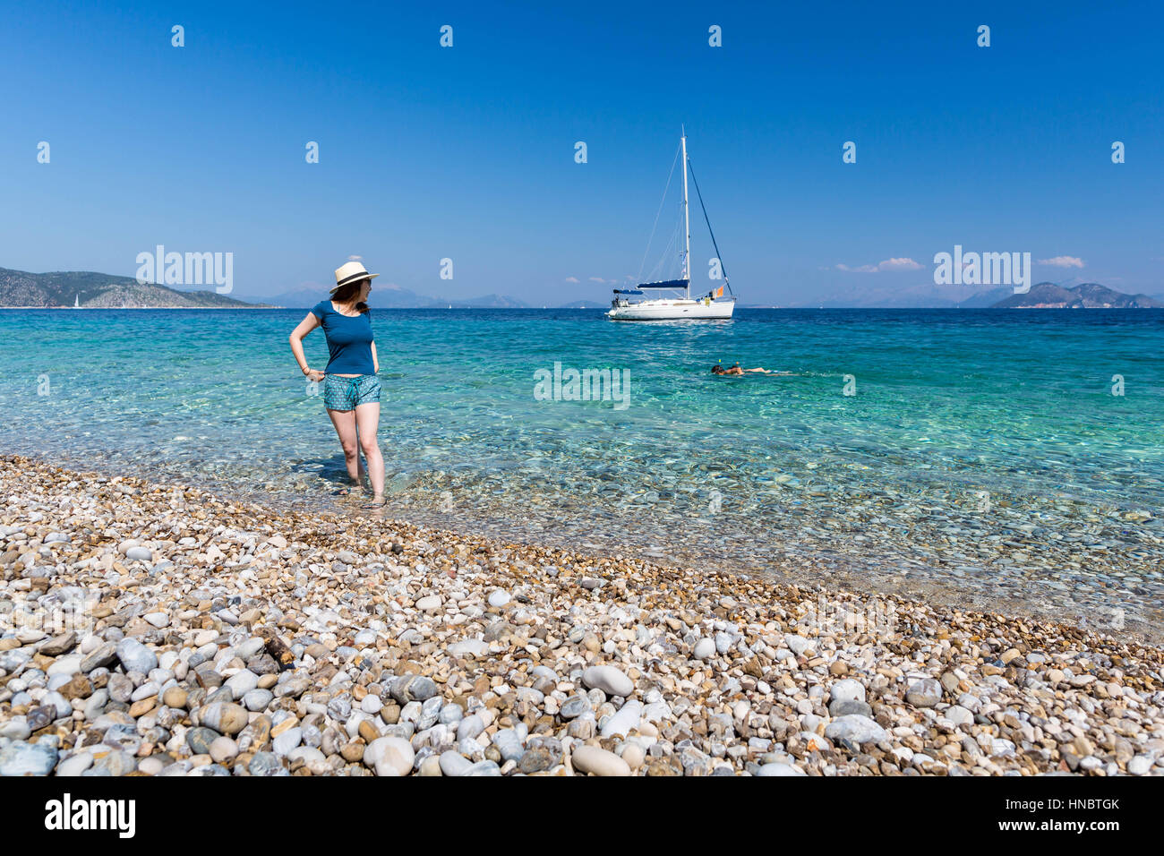 Woman standing in sea looking over her shoulder at couple swimming, Ithaki, Greece Stock Photo