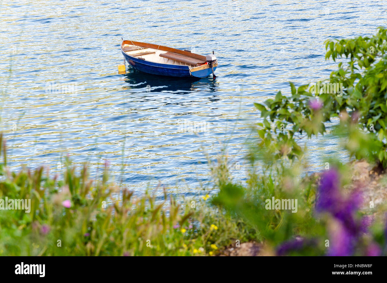 Empty blue boat moored in crisp clear waters of lake, river or sea Stock Photo