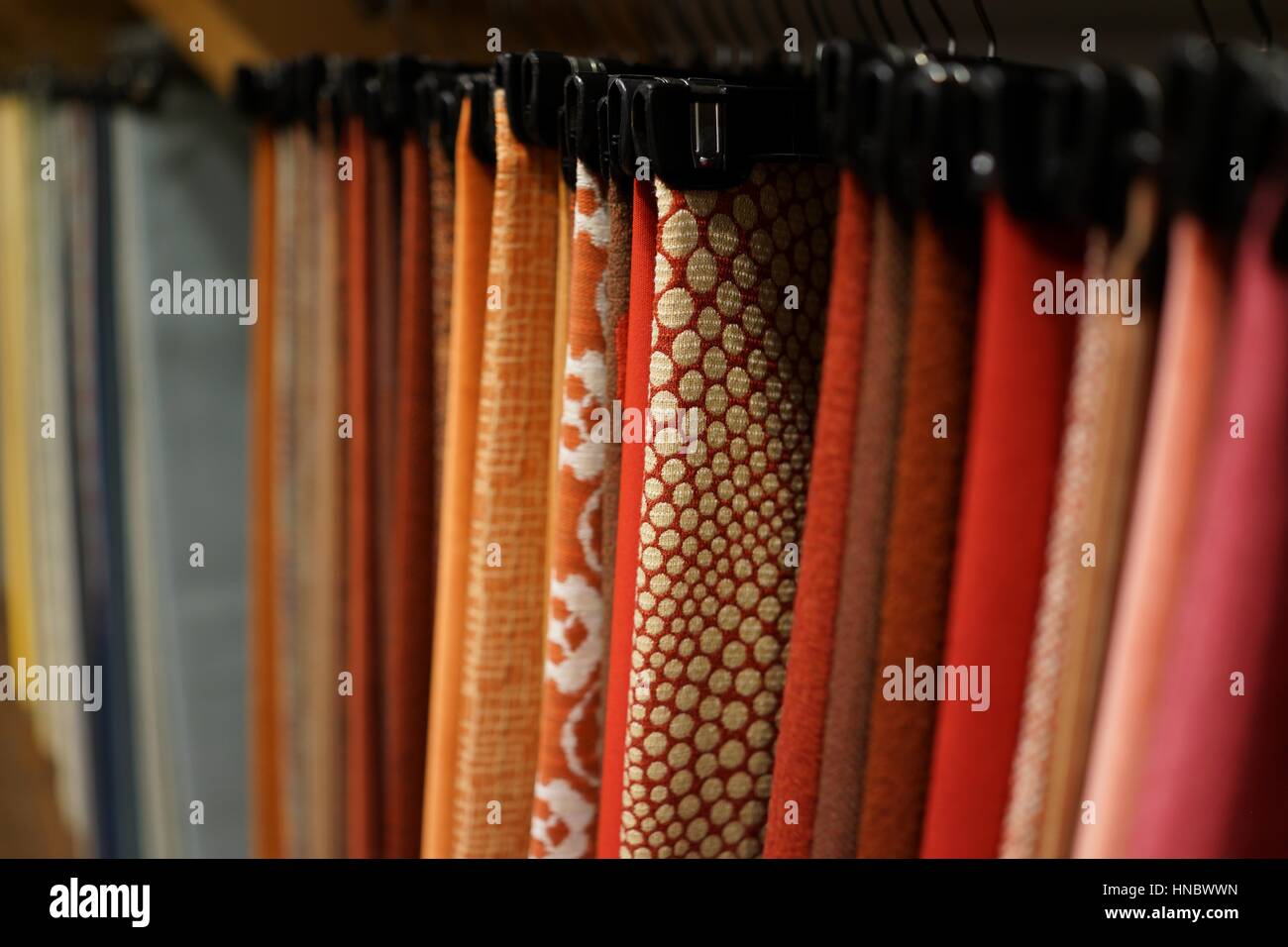 A rack of  patterned upholstery fabric samples hung closely together on black plastic hangers, solid colors and patterns, reds, pink, ochre, blue hues Stock Photo