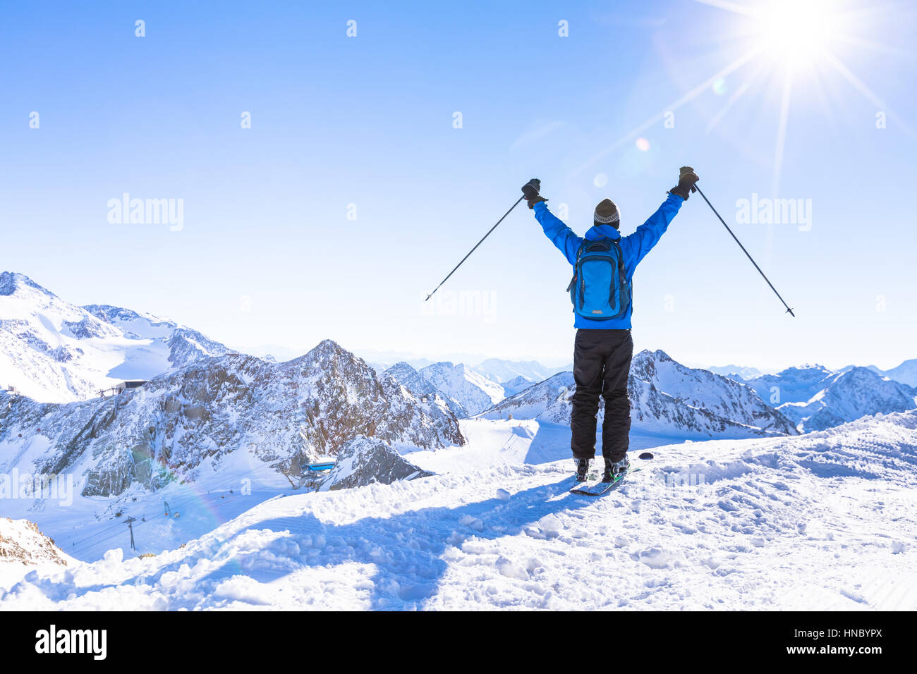 Back view of a happy skier with raised hands as a symbol of victory looking at a panoramic view of the snow white mountain landscape around Stock Photo