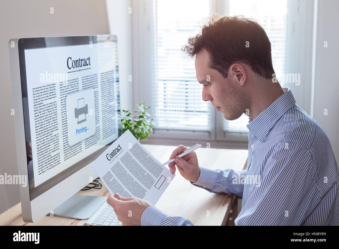 Young businessman signing a contract and reading the terms and conditions in the office. Modern interior with computer Stock Photo