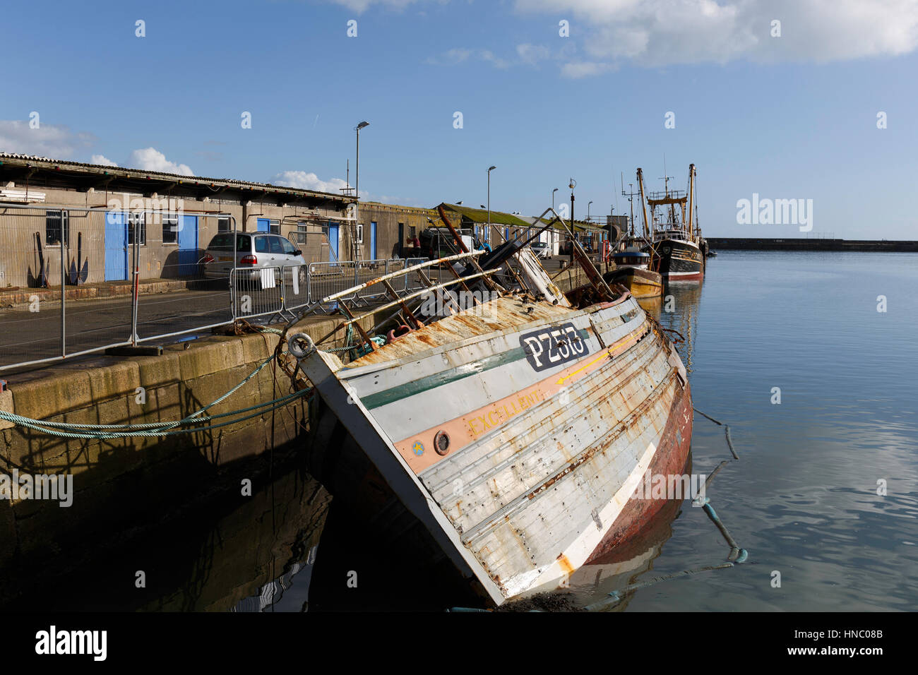 A line of derelict and decommissioned Fishing Boats lie alongside the east quay wall at Newlyn harbour Stock Photo