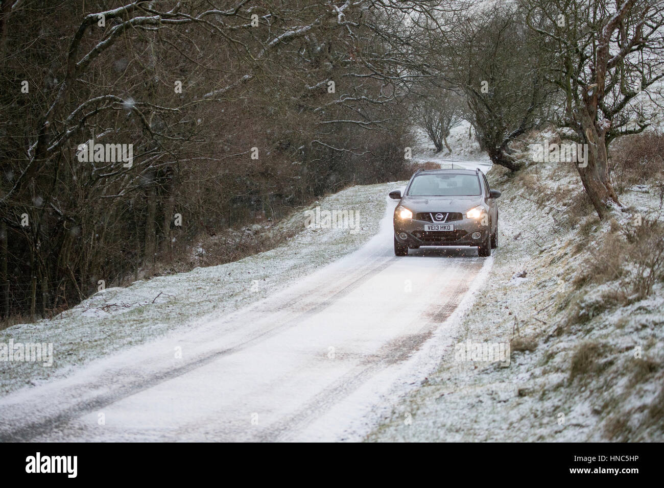 A car gingerly travels through blizzard conditions along a narrow lane