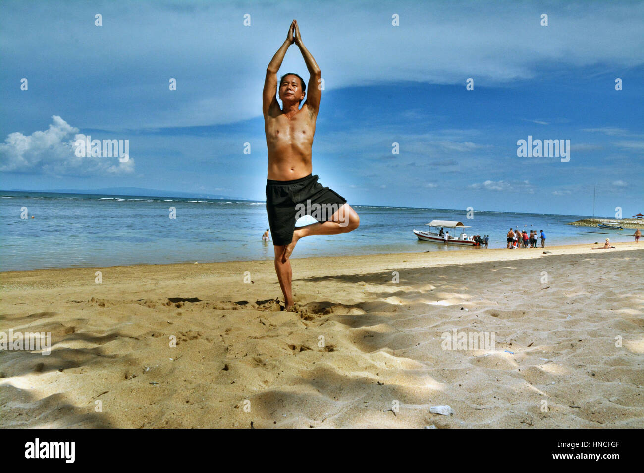 Baby Boomer Asian Male Exercises with Hatha Yoga Tree Pose on Sandy  Tropical Beach with Beautiful Blue Sky and Light Clouds Stock Photo - Alamy