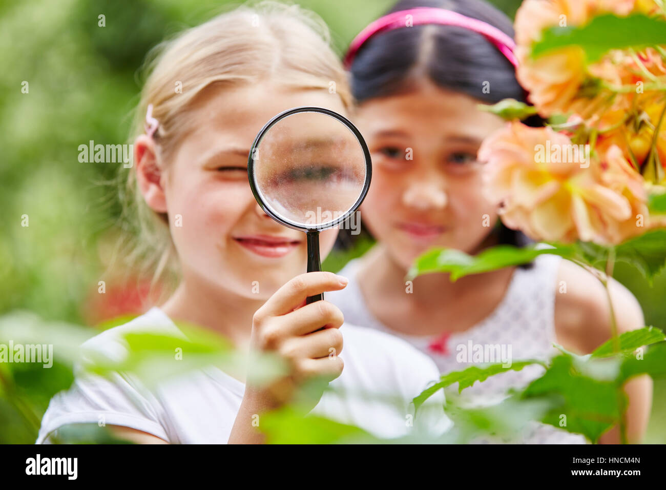 Children looking at flowers with curiosity using magnifying glass in nature Stock Photo