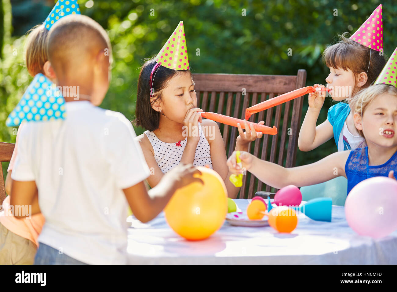 Kids celebrate together at garden party in summer with balloons and noise makers Stock Photo