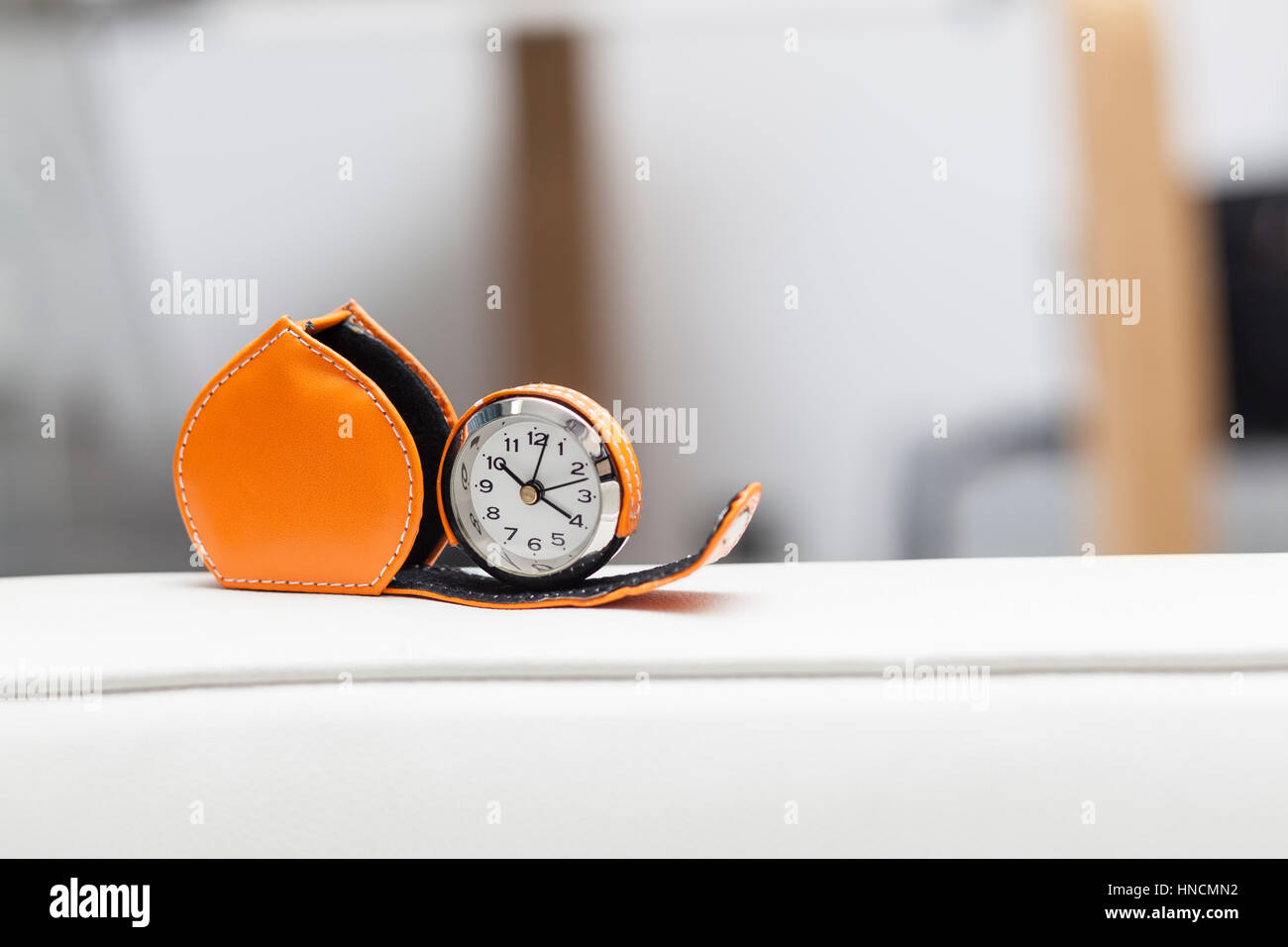 Small pocket watch with leather orange case on white surface, isolated with blurred background office style Stock Photo