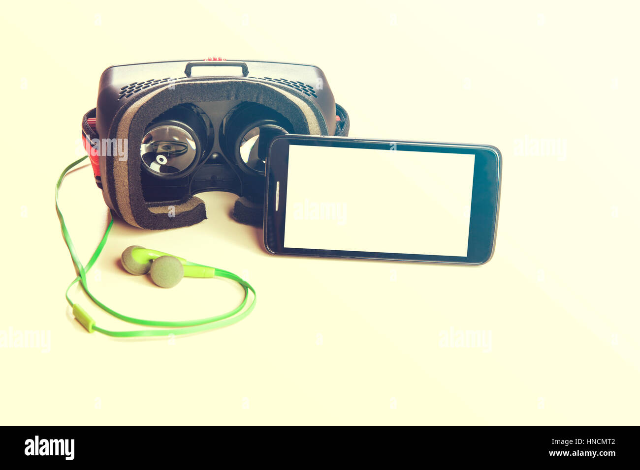 Virtual reality glasses for mobile phone, with smart hone with blank screen and green headphones on white table, space for app or website screenshot Stock Photo