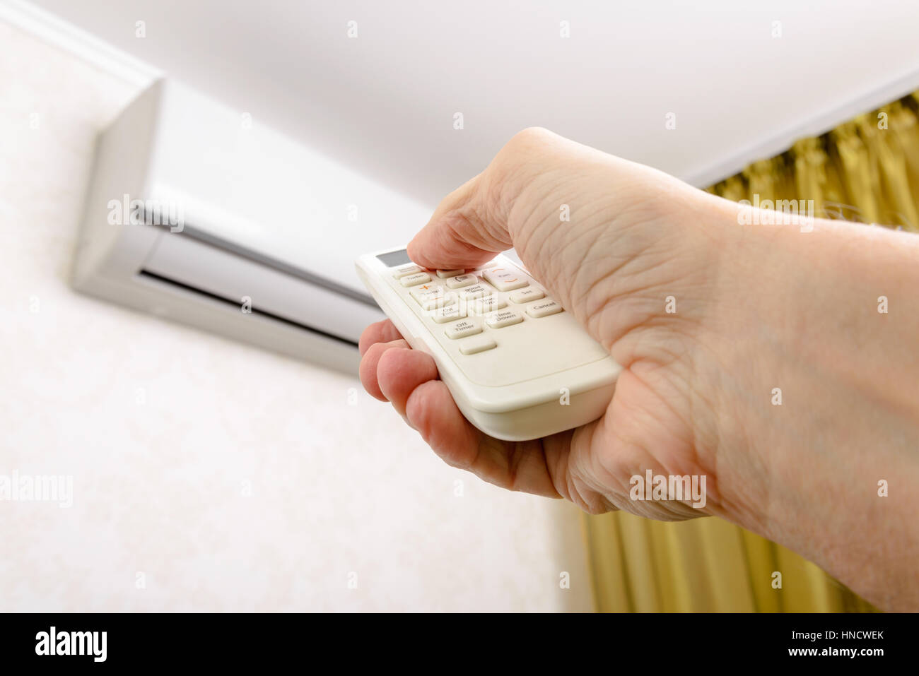 A man holds a remote control in his hand to pilot a wall-mounted air conditioner Stock Photo