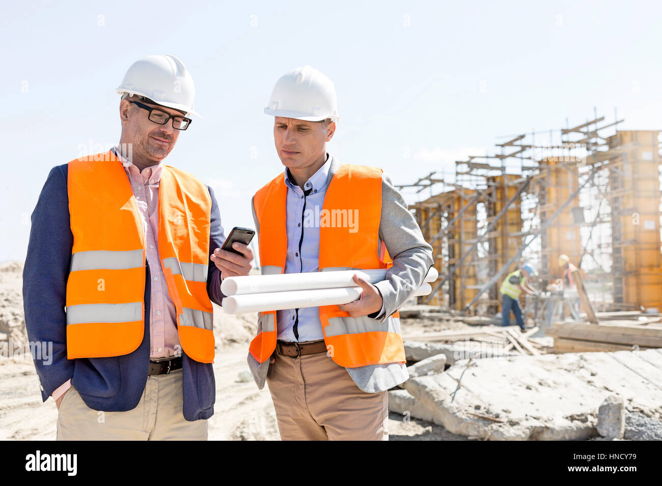 Male engineers using mobile phone at construction site against clear sky Stock Photo