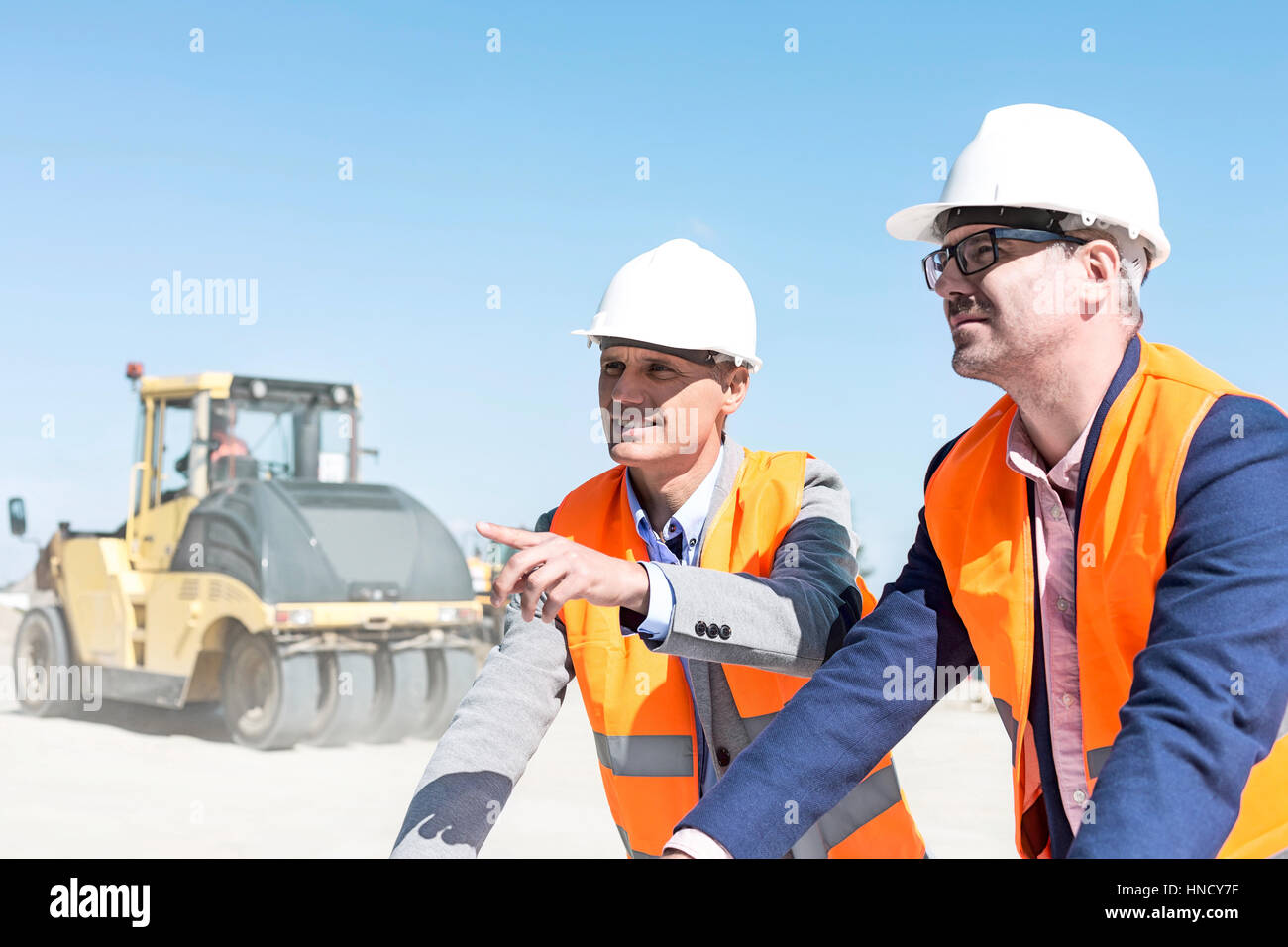 Supervisor explaining plan to colleague at construction site against clear sky Stock Photo