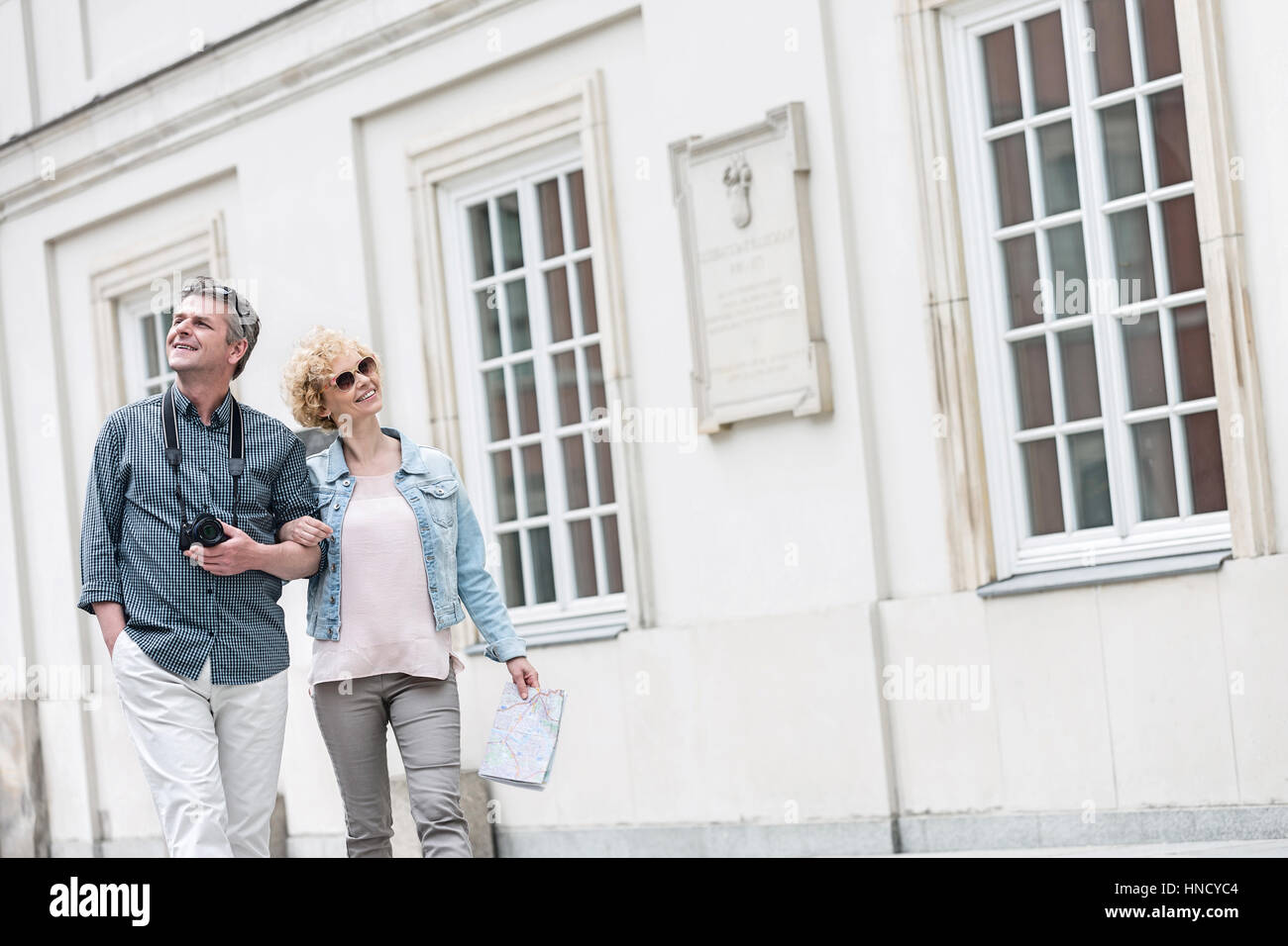 Happy middle-aged tourist couple walking arm in arm by building Stock Photo