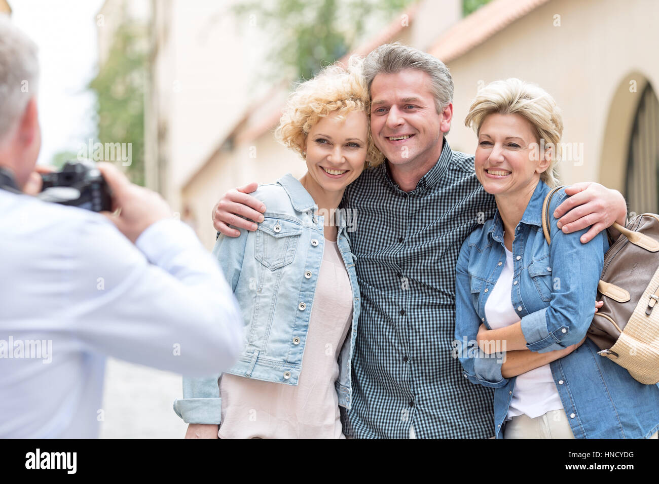 Rear view of man photographing male and female friends in city Stock Photo