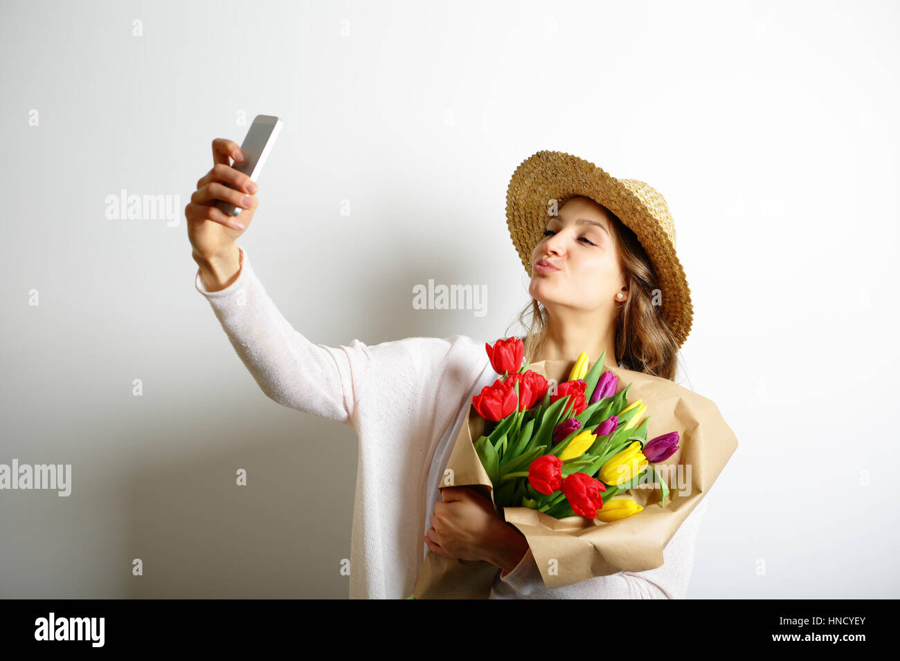 Young woman with kissing lips holding a bouquet of flowers in her hand, and makes selfie photo Stock Photo