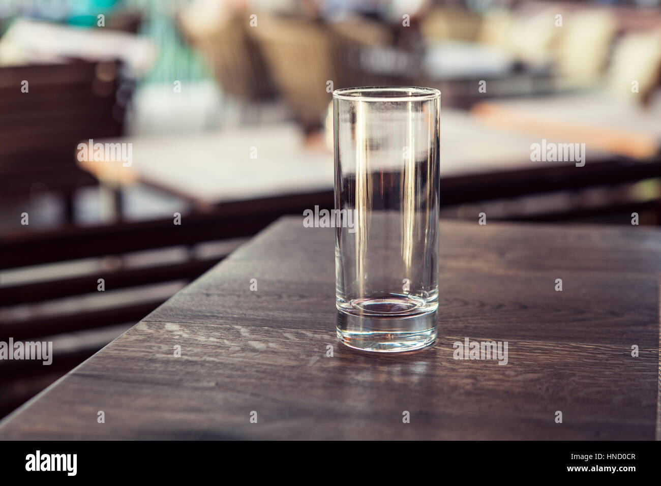Empty transparent cylindrical glass over wooden table at restaurant, outdoor terrace, extreme shallow of depth field,space for copy text Stock Photo
