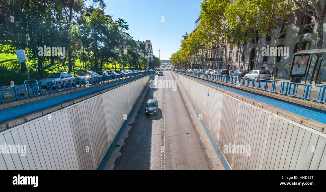 Sun shines bright on Calle del Alfonso where it enters a tunnel that runs under an intersection, above.  Car travels down Alfonso XII Street toward tu Stock Photo