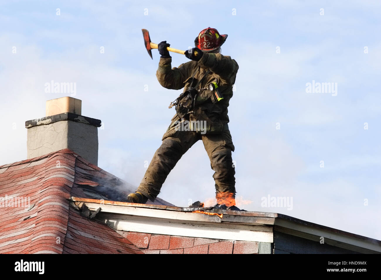 Firefighter chops a hole in the roof of a house that is on fire Stock