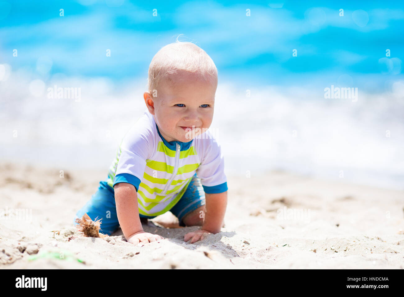 Little baby boy wearing blue rash guard suit playing on tropical ocean