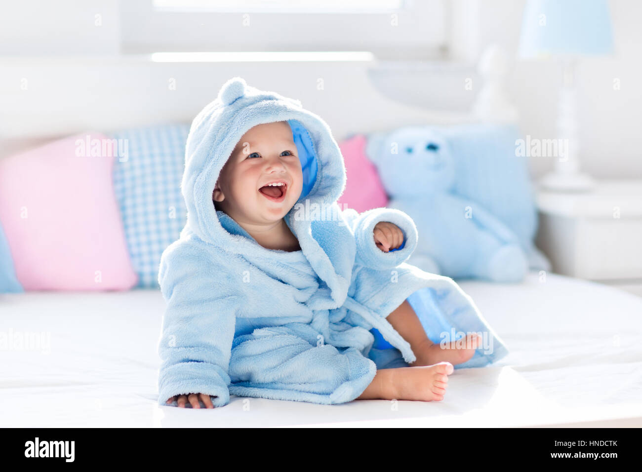 Cute happy laughing baby boy in soft bathrobe after bath playing on
