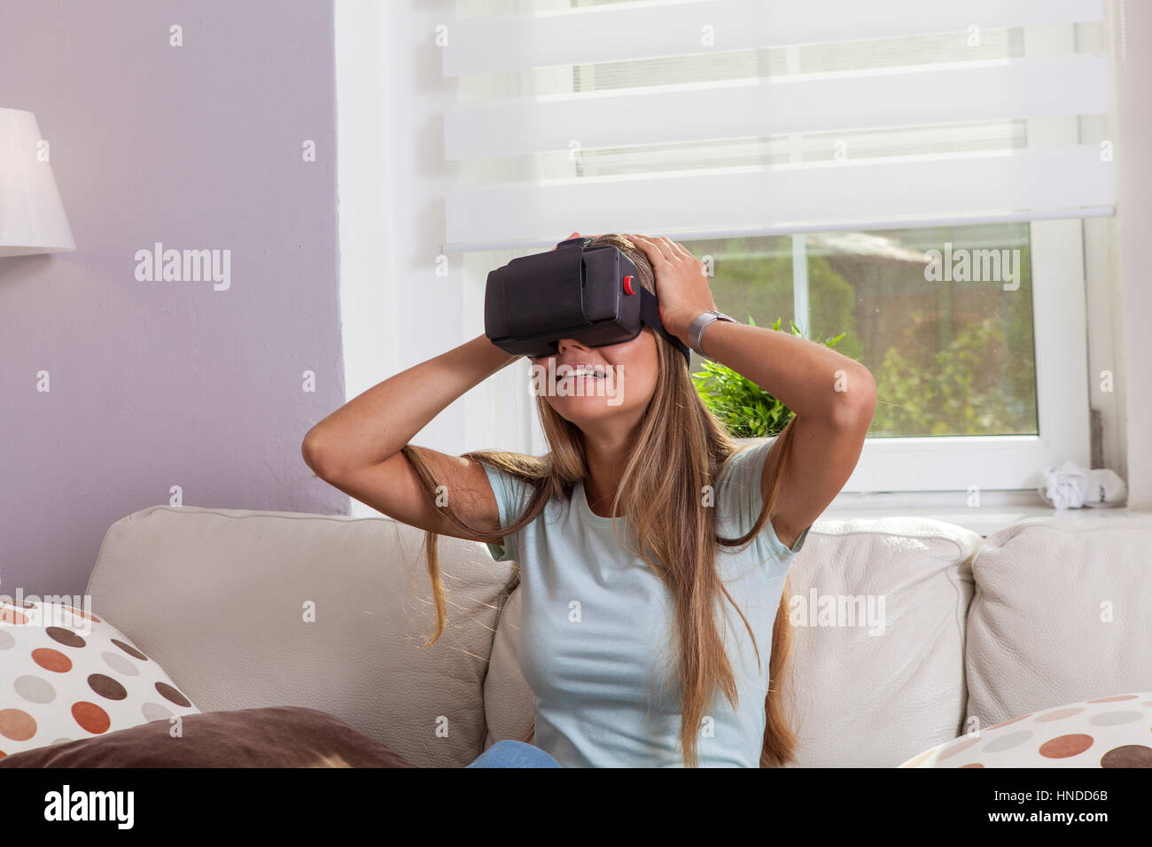 Girl seated on the couch playing with virtual reality headset got scared and put her hands on the head Stock Photo
