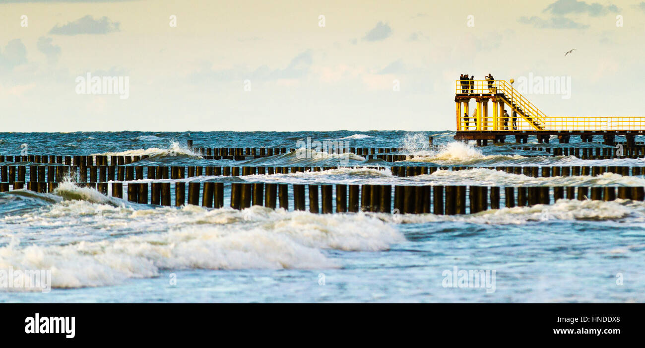 Yellow pier with people / tourists. Breakwaters and big waves. Stock Photo