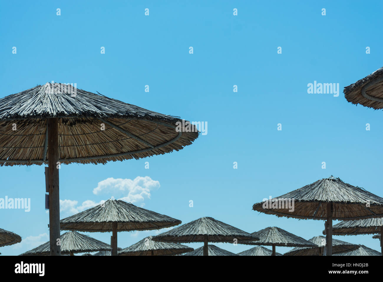 Abstract and conceptual summer, thatched umbrellas or wicker. With blue sky and white clouds on a Mediterranean beach. Stock Photo