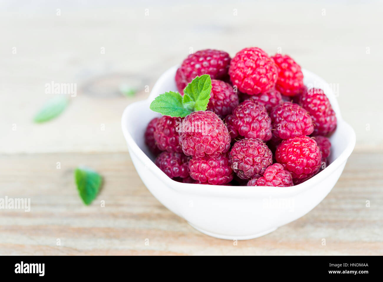 Close-up of fresh raspberry fruits in a white bowl on wooden table with copy space. Stock Photo