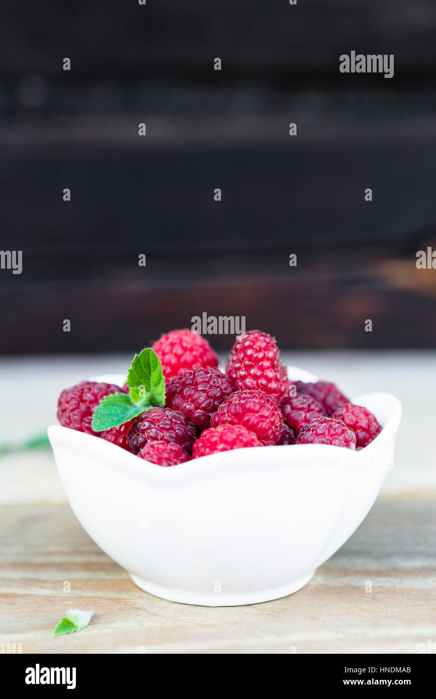 Close-up of fresh raspberry fruits in a white bowl on wooden table with copy space. Stock Photo