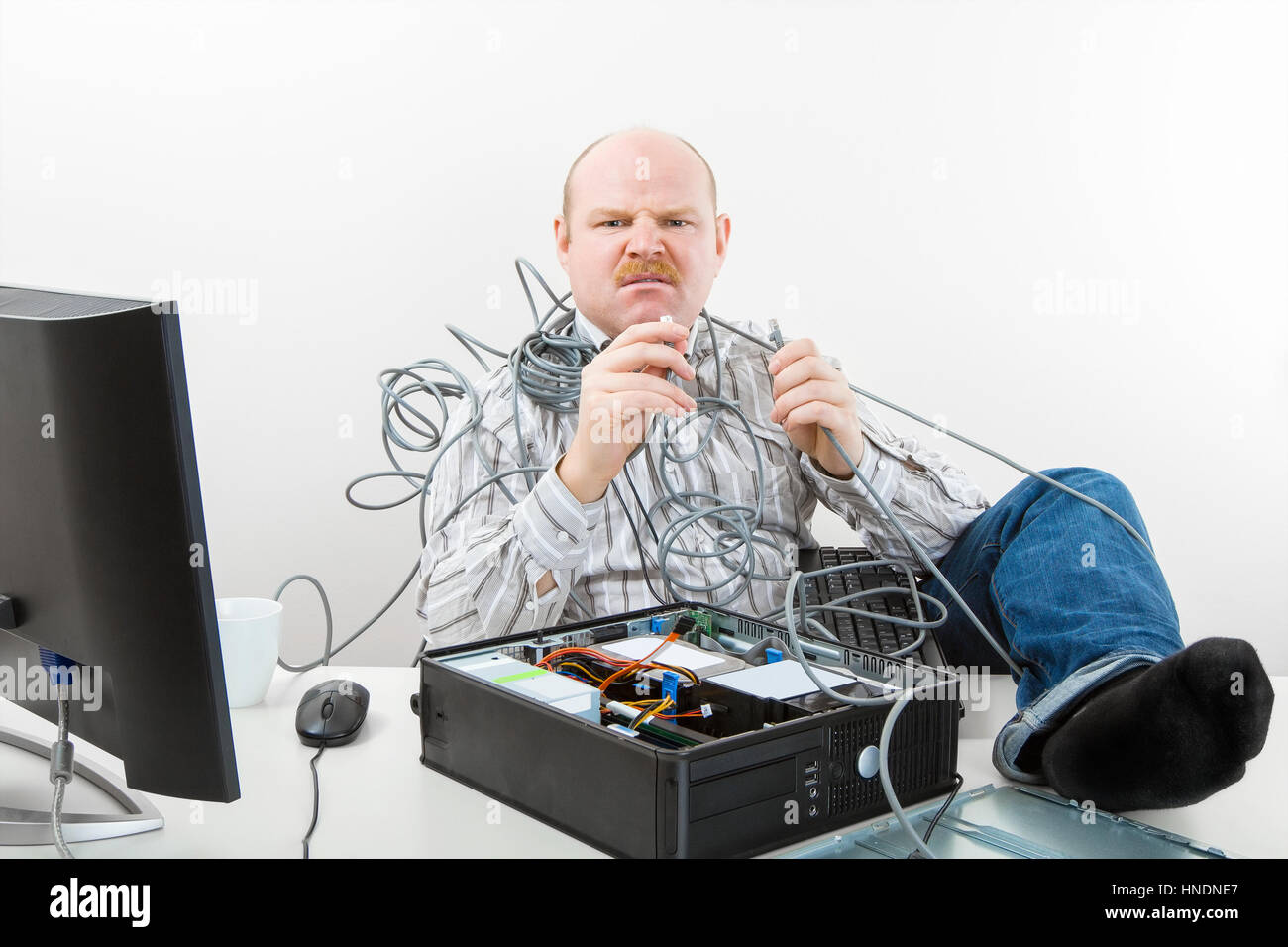 Furious Businessman Holding Tangled Cables Of Computer At Desk Stock Photo