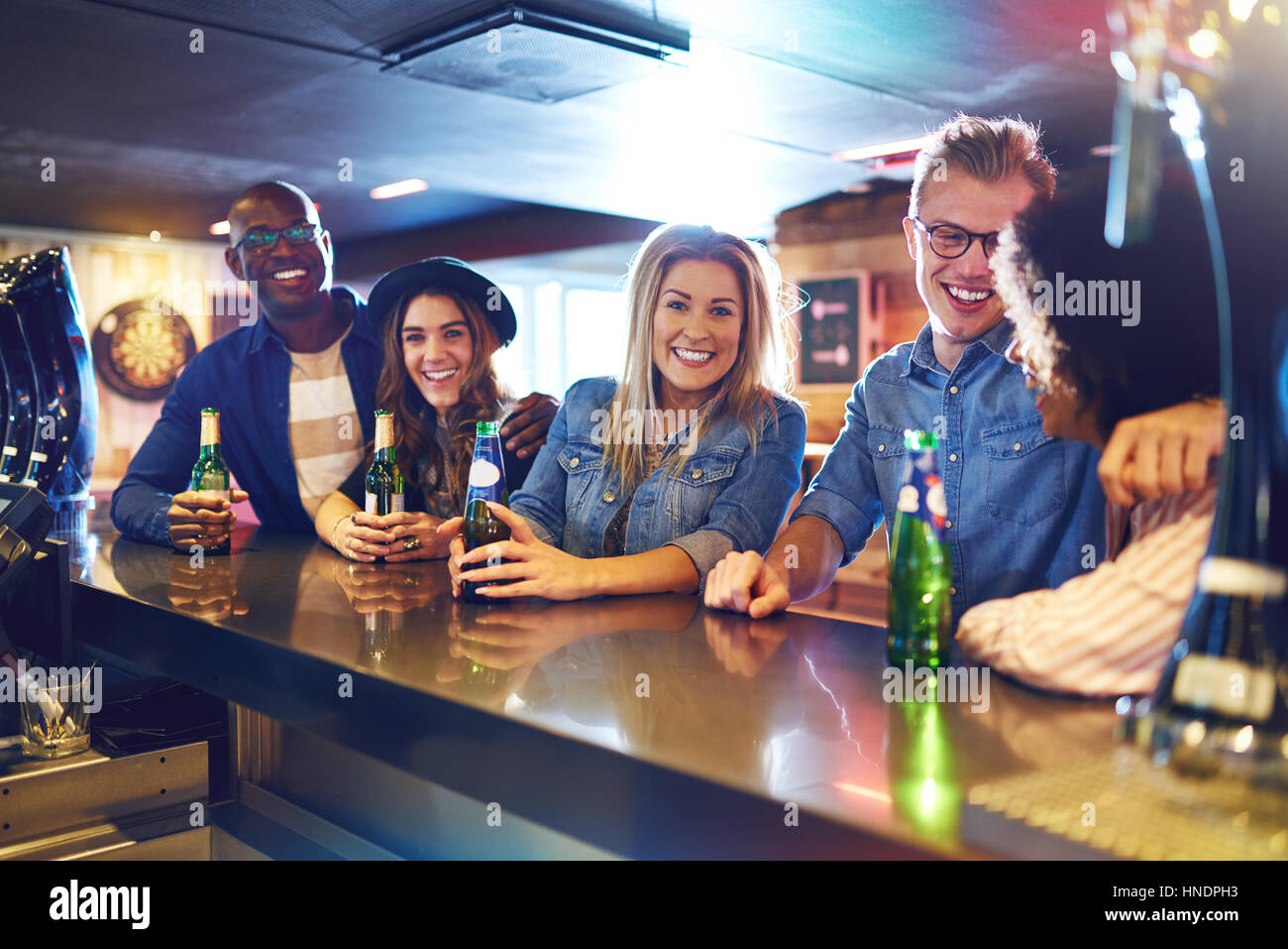 Horizontal shot of a smiling group of people looking at camera while drinking a beer in the bar. Stock Photo